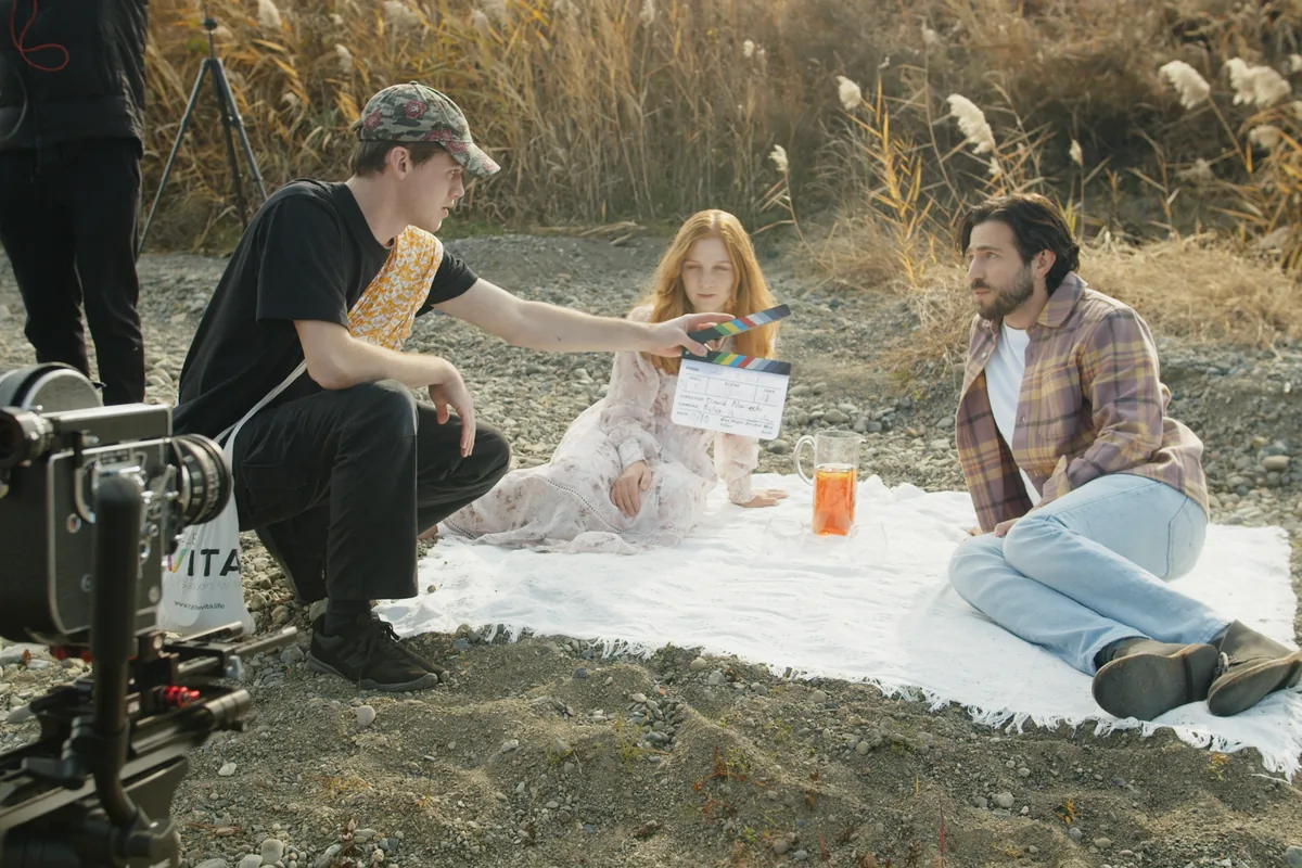Grant Hall holding a clapperboard beside two actors on an outdoor film set